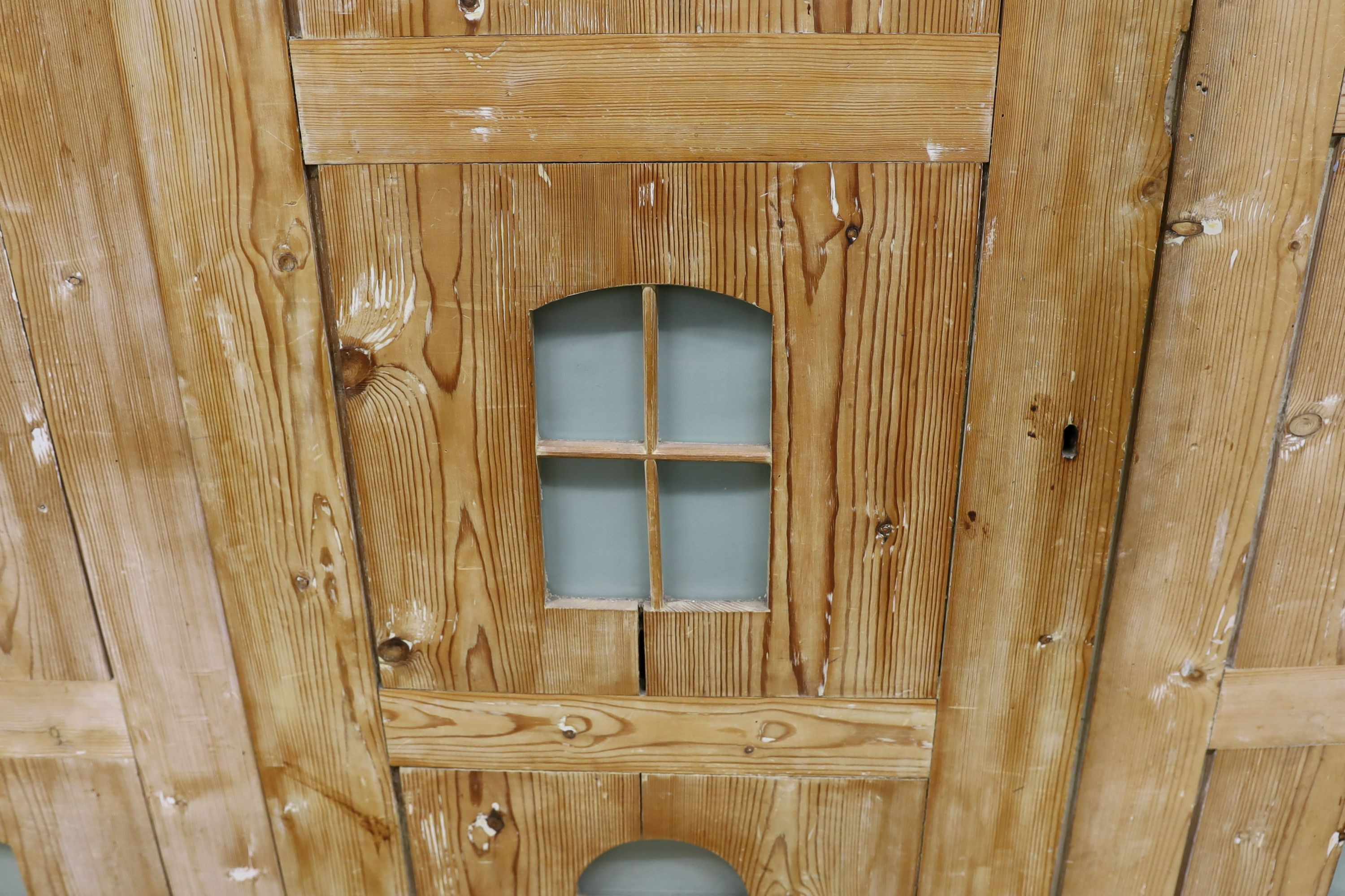 A 19th century stripped pine hall cupboard modelled as a dolls house the two door nine window facade enclosing a compartmented interior, width 182cm, depth 46cm, height 192cm